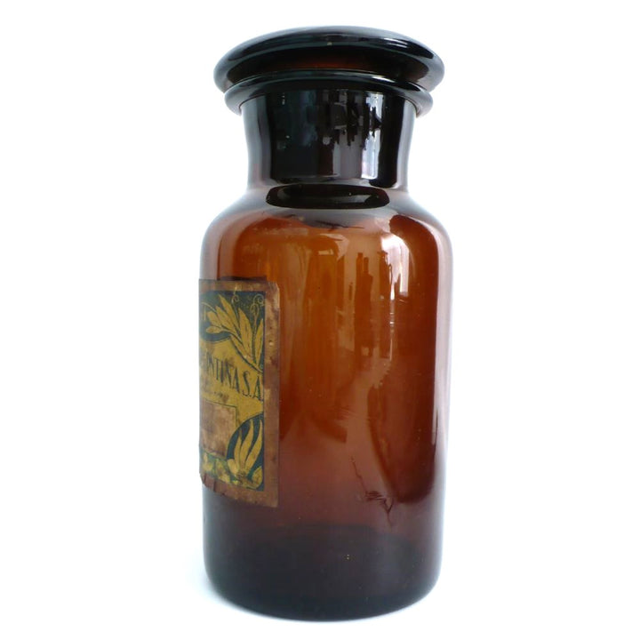 19th-century hand-blown amber glass apothecary jar with a label indicating it once contained cardamon seed powder. The jar has a dark amber color, a narrow neck, and a round stopper.