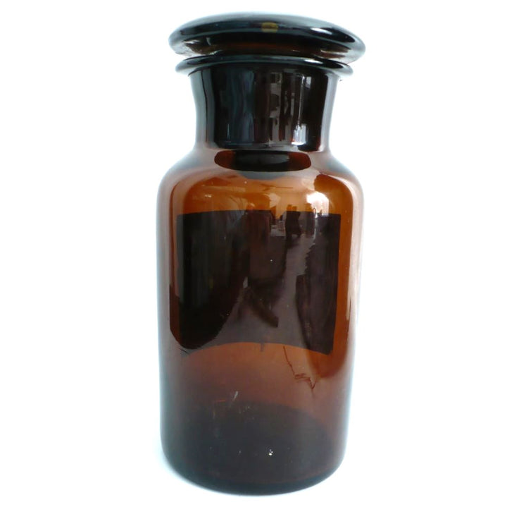 19th-century hand-blown amber glass apothecary jar with a label indicating it once contained cardamon seed powder. The jar has a dark amber color, a narrow neck, and a round stopper.