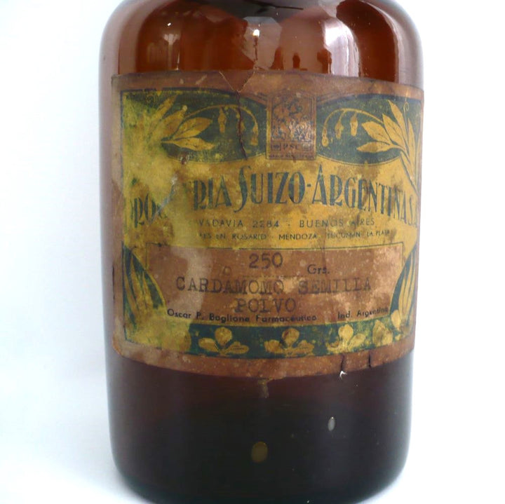 Original paper label of 19th-century hand-blown amber glass apothecary jar with a label indicating it once contained cardamon seed powder. The jar has a dark amber color, a narrow neck, and a round stopper.