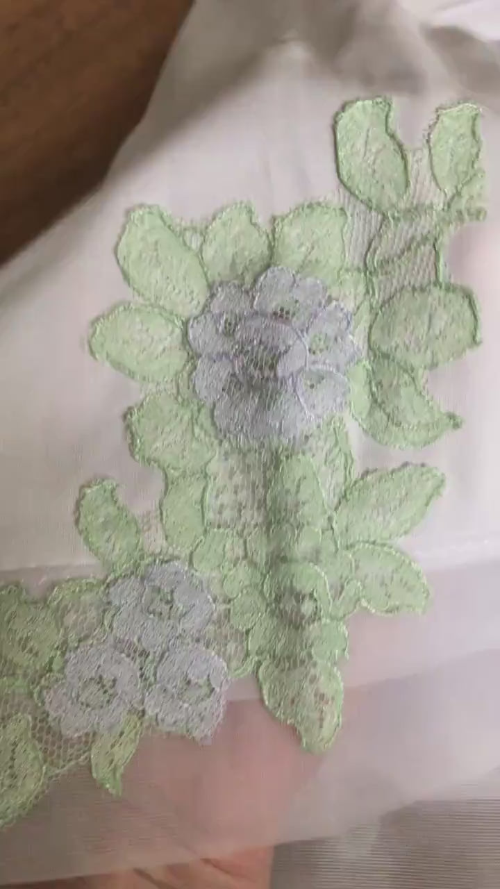 A close up view of the pastel purple flower with light green leaves lace applique at the hem. It has a pretty light-catching sheen to it. Feminine, yet classy.