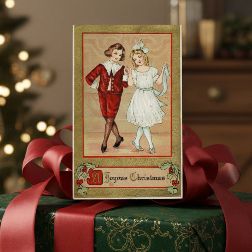 1915 A Christmas Country Dance Gilded Embossed Vintage Postcard on a wrapped gift with a blurred Christmas tree in the background