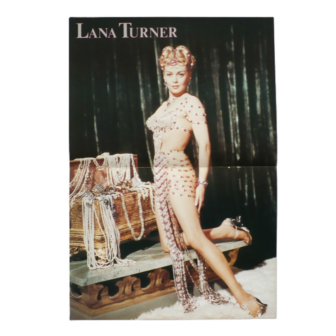 An original vintage Lana Turner magazine centerfold pin-up poster of The Prodigal  featuring Lana Turner posing in a beaded belly-dance-inspired outfit, seated beside a draped trunk against a dark curtain backdrop. The text 'LANA TURNER' appears at the top.