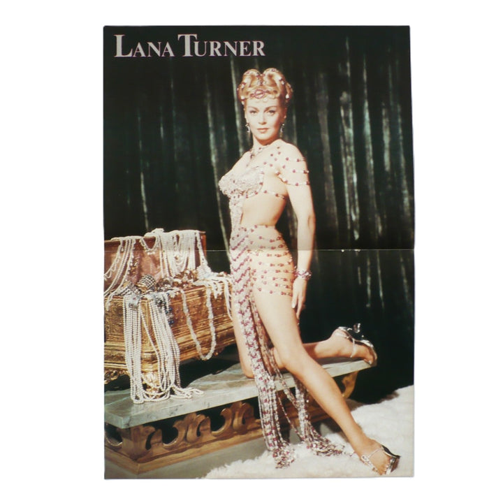 An original vintage Lana Turner magazine centerfold pin-up poster of The Prodigal  featuring Lana Turner posing in a beaded belly-dance-inspired outfit, seated beside a draped trunk against a dark curtain backdrop. The text 'LANA TURNER' appears at the top.