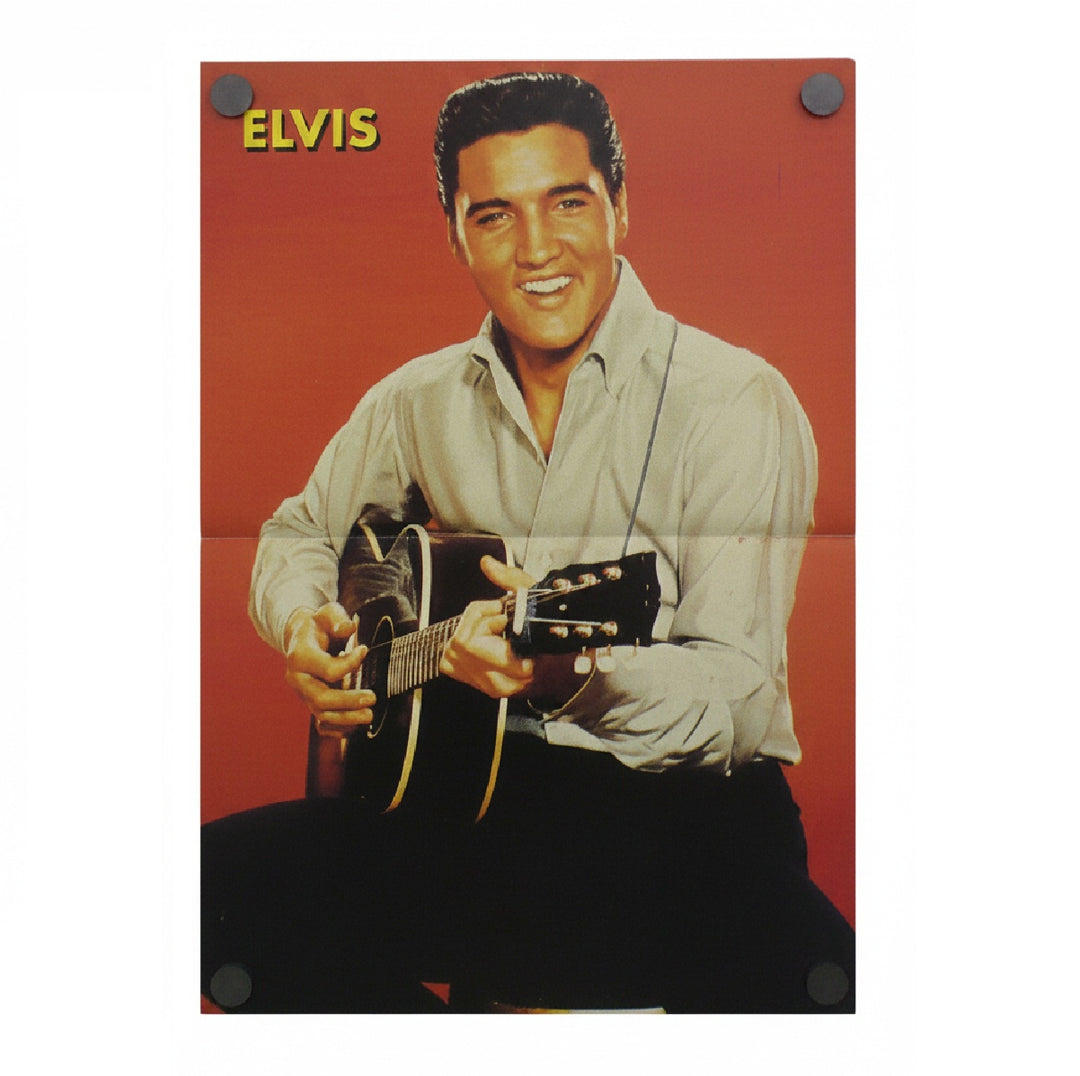 A vintage magazine poster of Elvis Presley holding an acoustic guitar against a red-orange background, with the name 'ELVIS' in yellow at the top. The poster is shown hanging with black binder clips visible in the corners.