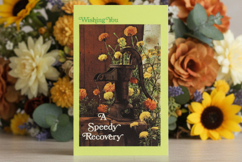 Greeting card with floral design and text 'Wishing You a Speedy Recovery' in front of a floral arrangement.
