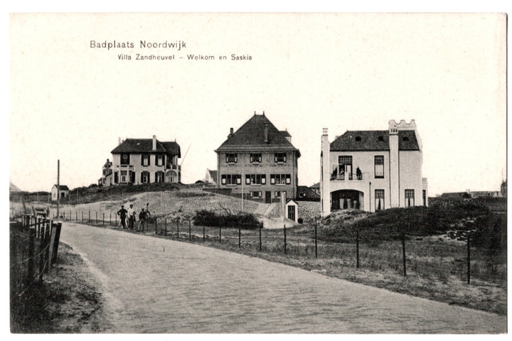 This antique monochromatic postcard features a scenic view of the seaside resort (Badplaats) of Noordwijk in the Netherlands. The image captures several grand villas situated on the dunes, including the identified Villa Zandheuvel, Villa Welkom, and Villa Saskia. A brick road winds through the foreground, with several figures standing near a fence line. 