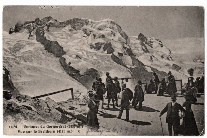 A panoramic view of the snow-covered Breithorn peak (4171 meters) in the Swiss Alps near Zermatt. A diverse group of early twentieth-century travelers in period attire, including men in bowler hats and women in long dresses, are seen congregating at the summit. One individual is looking through a mounted telescope.