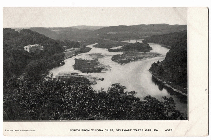 an expansive northward view of the Delaware River from Winona Cliff at the Delaware Water Gap in Pennsylvania. The image shows the river winding through the gap with several small islands visible in the stream. On the left hillside, the Kittatinny House resort hotel is perched overlooking the valley.