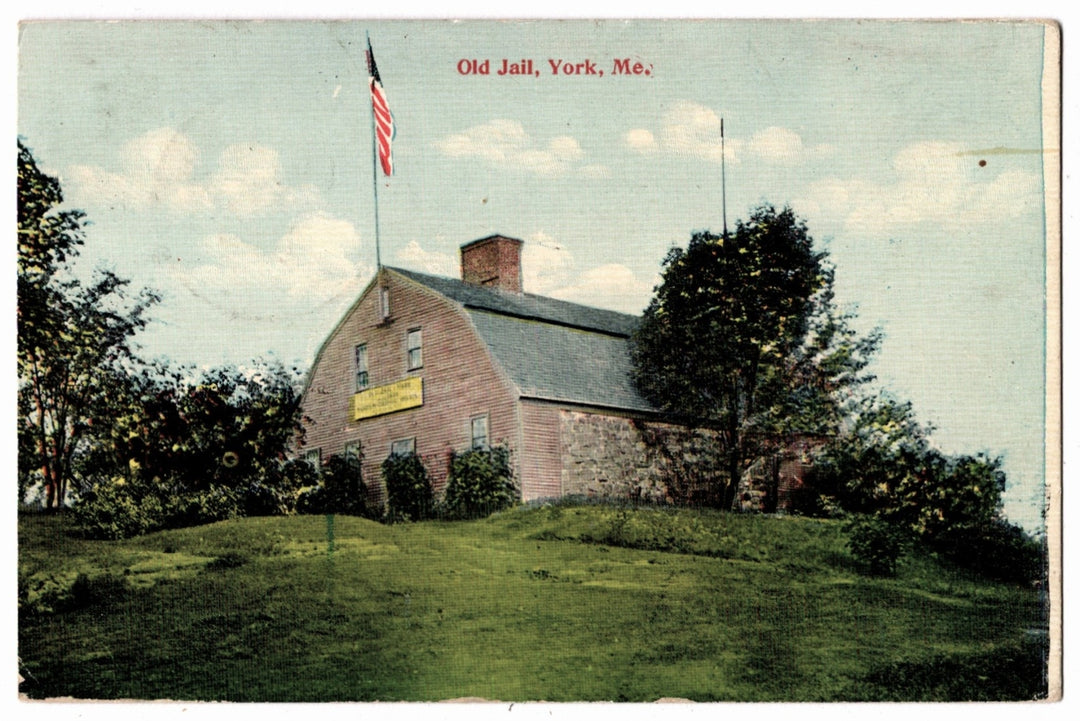 Old brick building with a flag on top, labeled 'Old Jail, York, ME', surrounded by trees and grass. 1907 Old Gaol Museum York Maine Vintage Postcard.