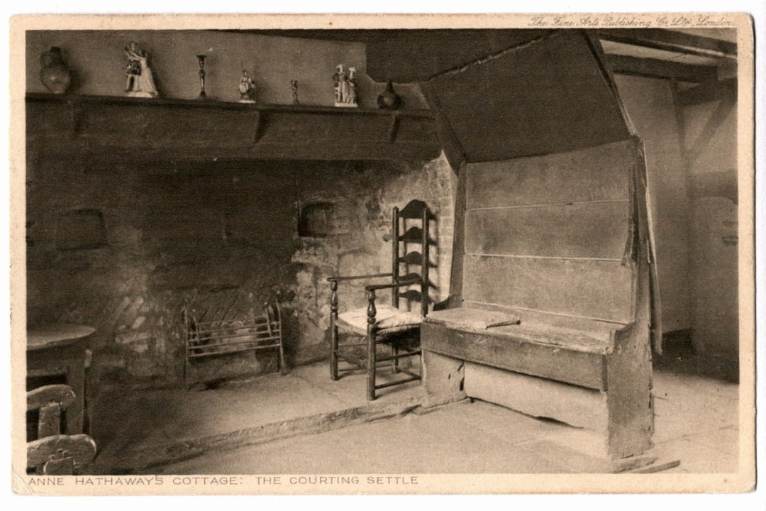 Vintage black and white photo of a rustic interior with wooden furniture and a fireplace. 1920s Anne Hathaway's Cottage England Vintage Postcard.