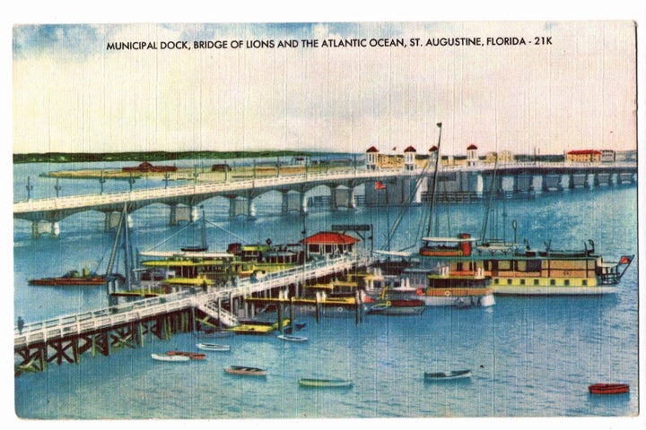 Vintage postcard of a dock with boats and a bridge over water, labeled 'Municipal Dock, Bridge of Lions and the Atlantic Ocean, St. Augustine, Florida'.