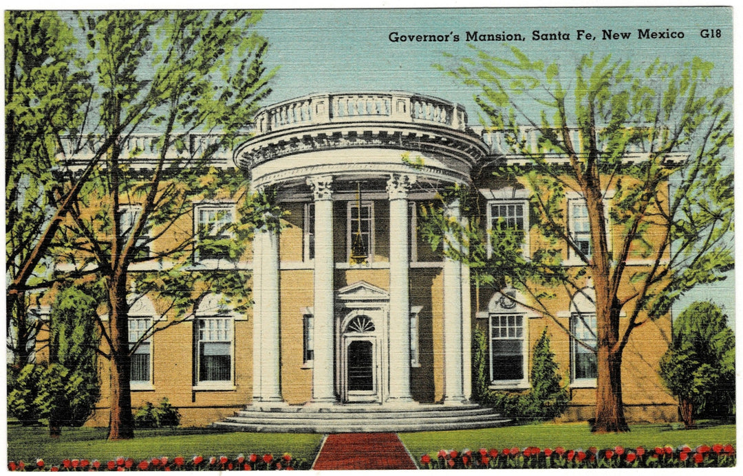 A vintage color linen postcard featuring the Governor's Mansion in Santa Fe, New Mexico. The two-story building is buff-colored with a grand, white, semi-circular neoclassical portico supported by four tall columns. The mansion is flanked by two large, leafy green trees. In the foreground, a red-paved walkway leads to the entrance, bordered by a row of red and white tulips. The sky above is a pale, clear blue, and the title "Governor's Mansion, Santa Fe, New Mexico G18" is printed in the upper right.