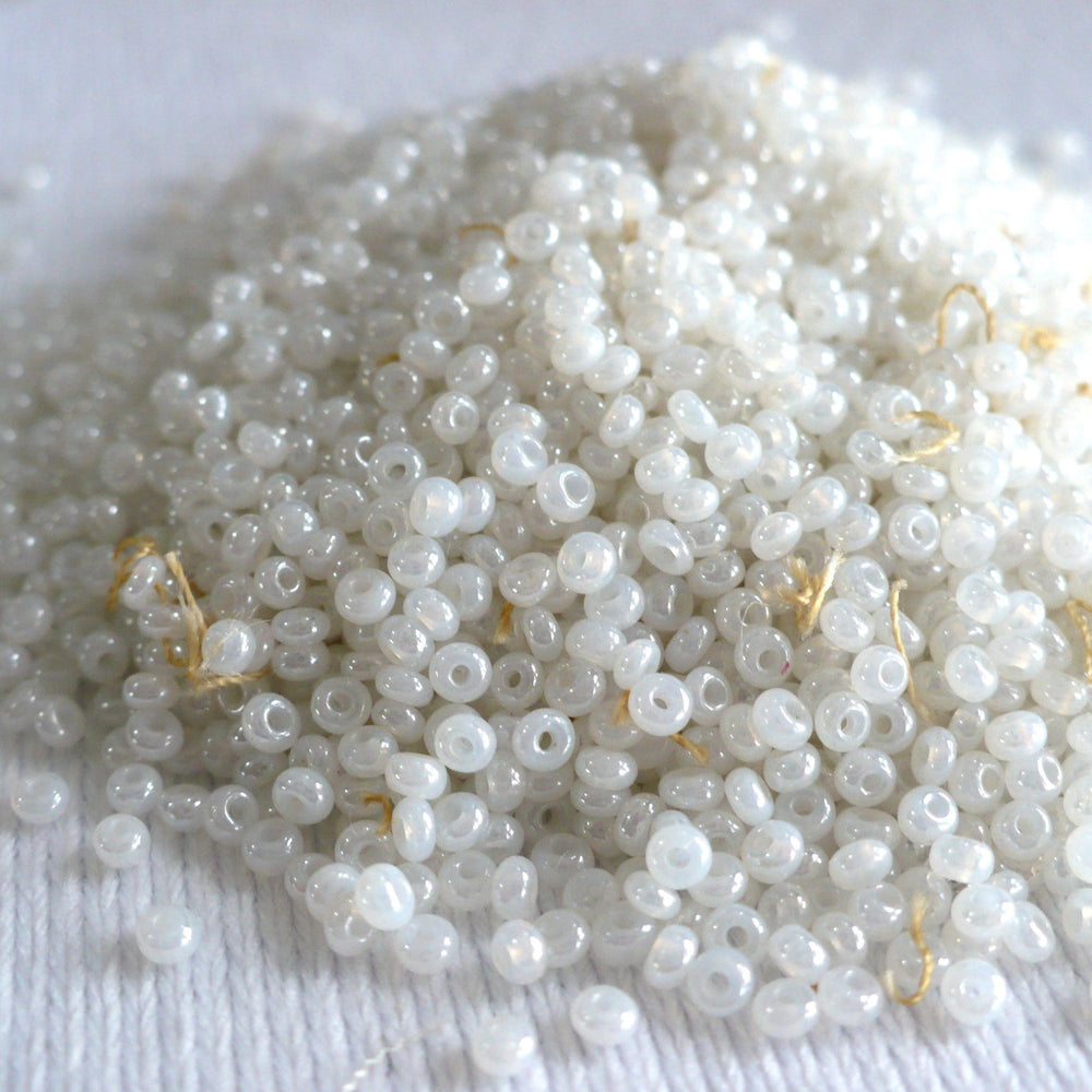 1920s White Ceylon Glass Seed Beads in a pile on white fabric background.