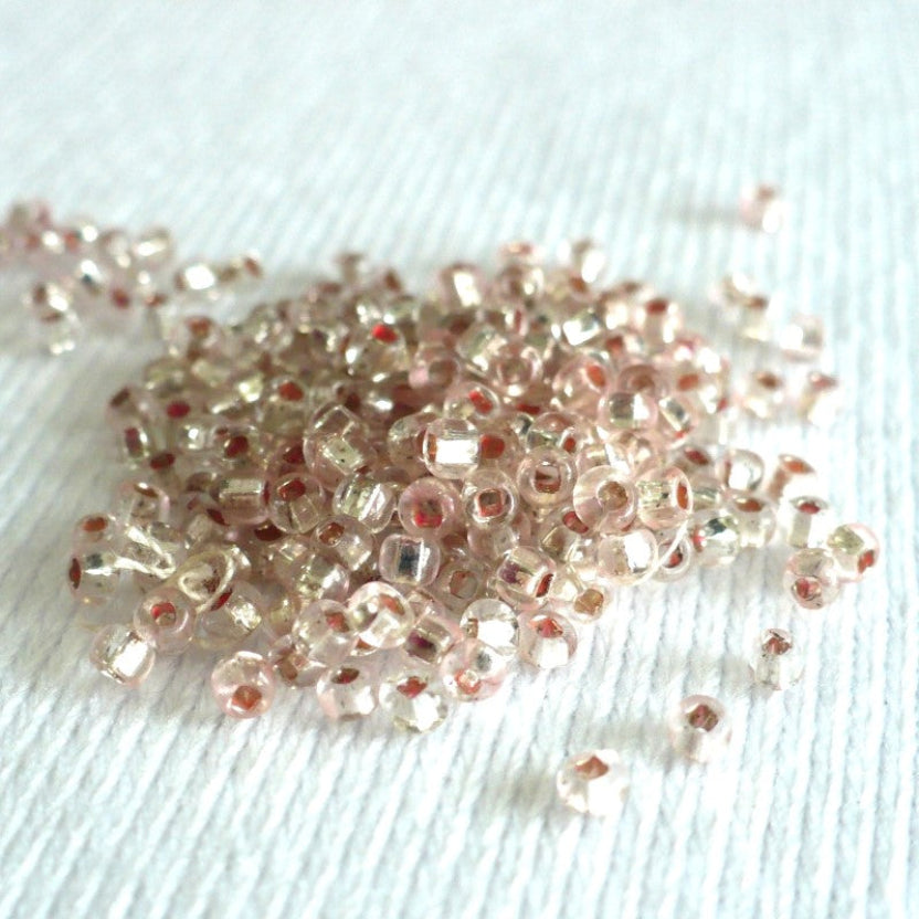 1920s Pink Mercury Glass Seed Beads on white fabric background.