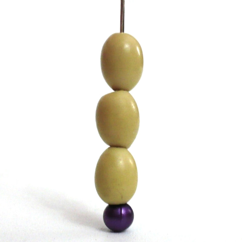 Batch 1910s 5x7mm Smooth Oval Vegetable Ivory Beads, close-up, strung on a stick pin.