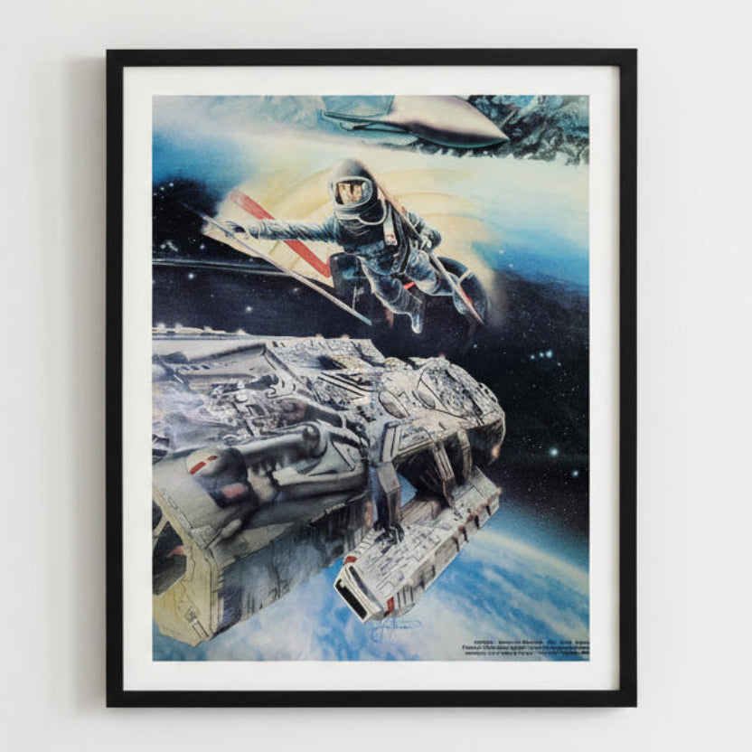 Framed artwork of a space scene with a spaceship and astronaut, on a white wall.