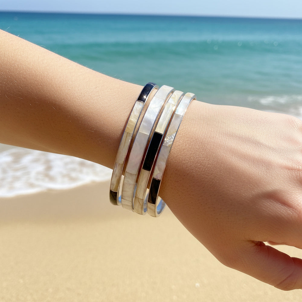 Hand wearing 1980 Set of 4 Abalone Shell Bracelet Set with a beach background.