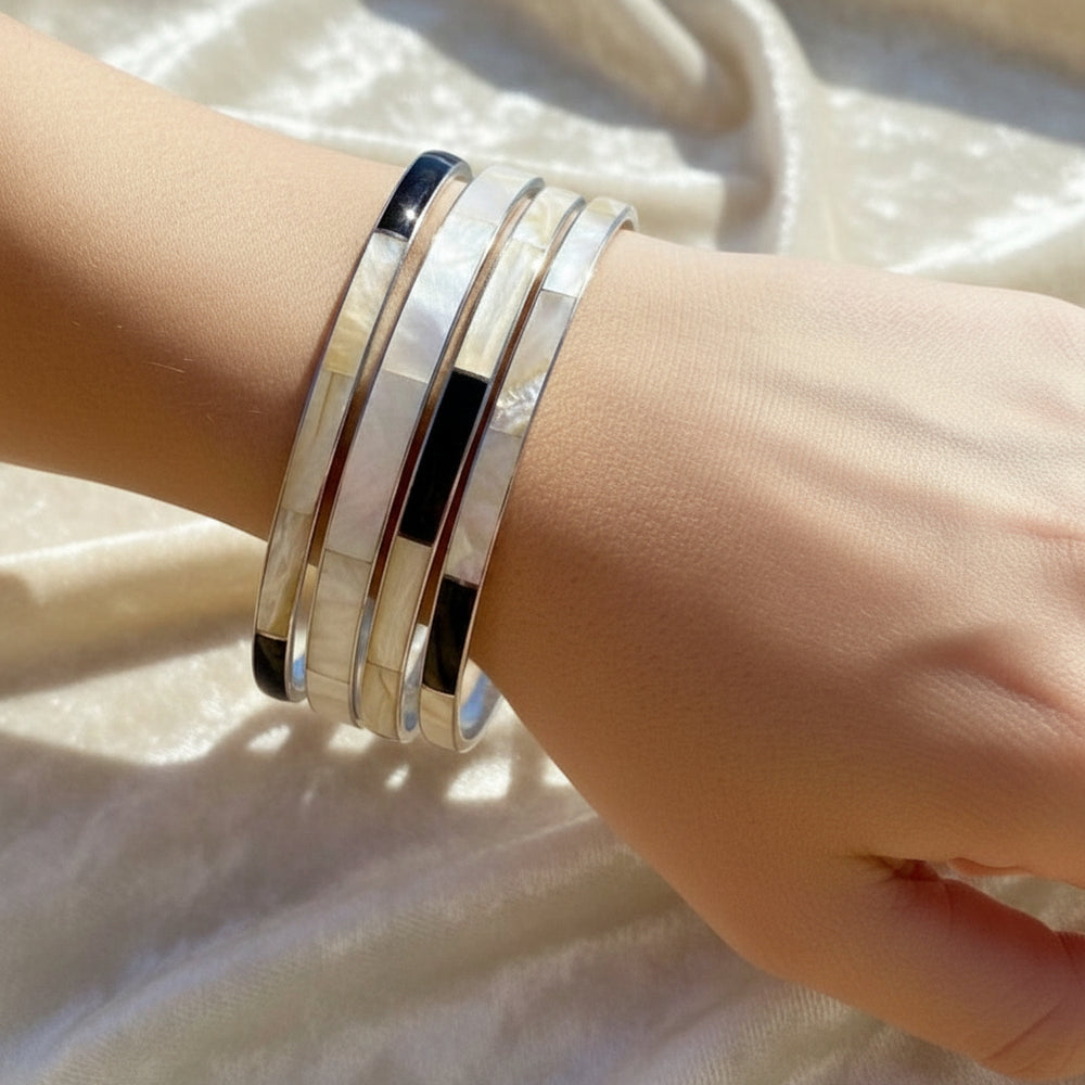 Four vintage mother of pearl stacking bracelets on wrist with white background.