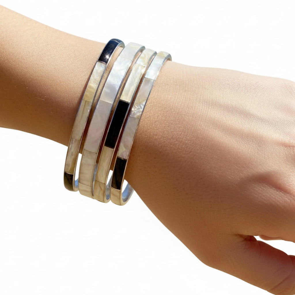 Four vintage mother of pearl stacking bracelets on wrist with white background.
