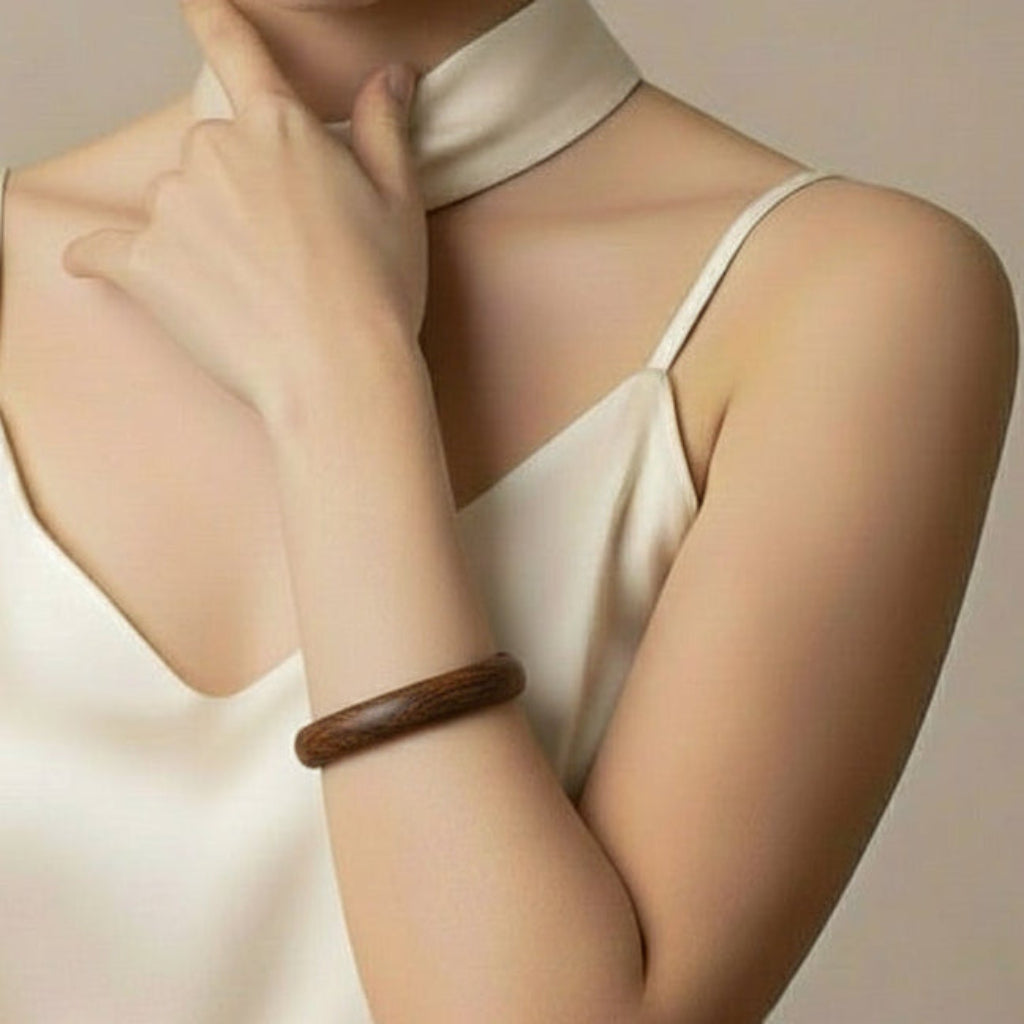 Woman wearing a white top with a wooden bracelet on her wrist against a neutral background