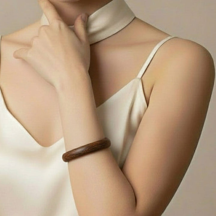 Woman wearing a white top with a wooden bracelet on her wrist against a neutral background