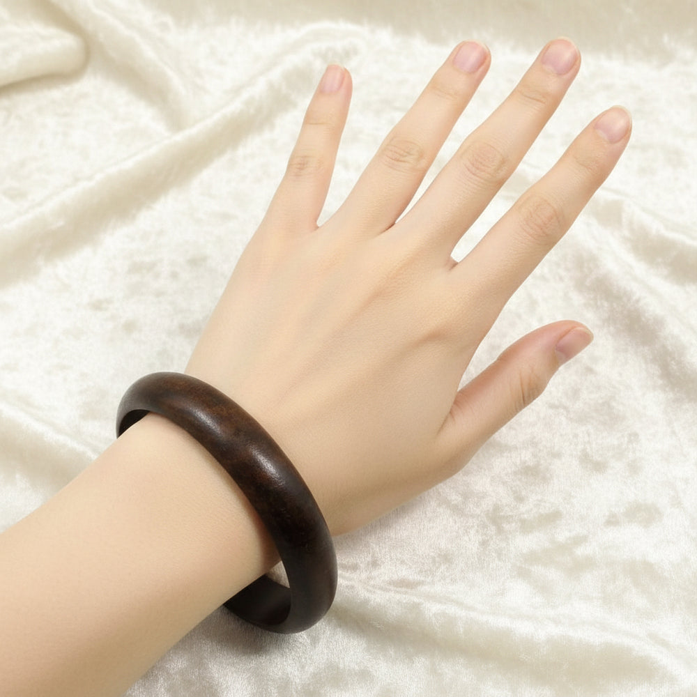 A 70s vintage dark teak wood bangle bracelet on a mannequin wrist with a white background.