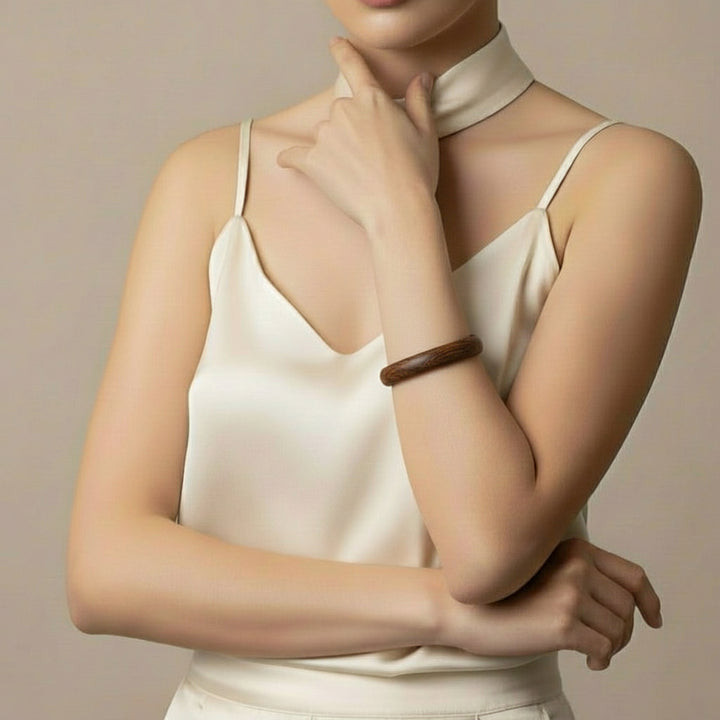 A 70s vintage dark teak wood bangle bracelet worn by a woman in cream colored silk camisole.