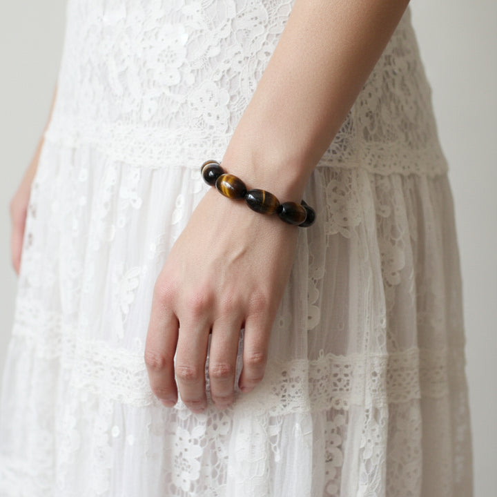 Bracelet with tiger eye  beads on a wrist against a white lacy gypsy skirt.