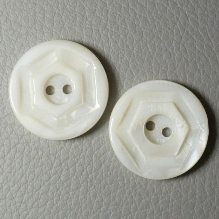 Two round opaque white glass buttons with a molded geometric pattern, displayed on a textured gray surface. faces front.