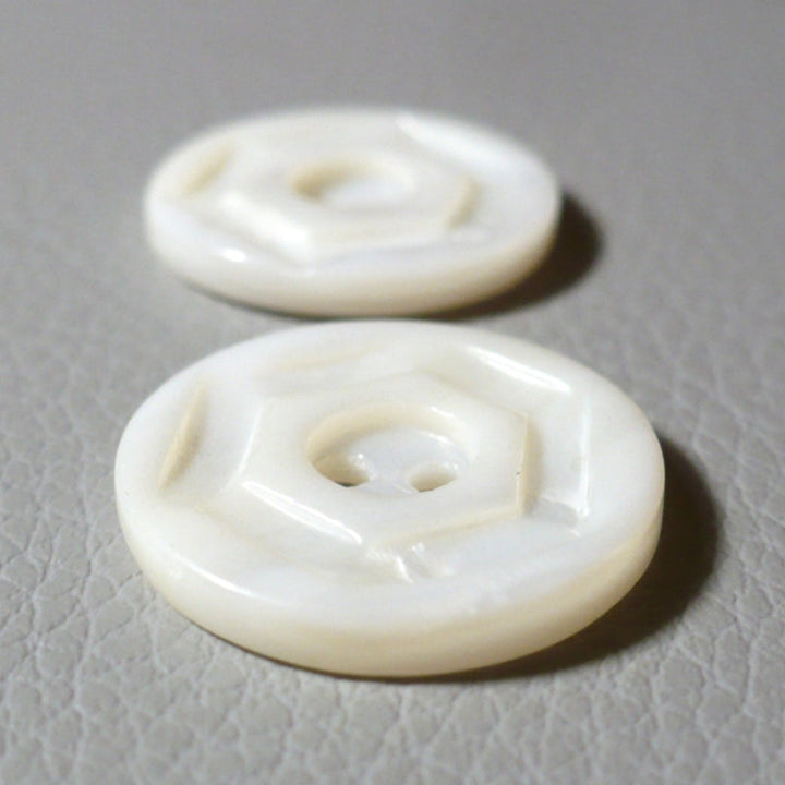 Two round opaque white glass buttons with a molded geometric pattern, displayed on a textured gray surface.