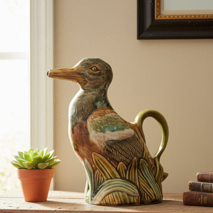 Decorative ceramic duck pitcherFrie Onnaing Majolica Duck Pitcher – “Canard dans les Roseaux” c.1910surface with a plant and books in the background.