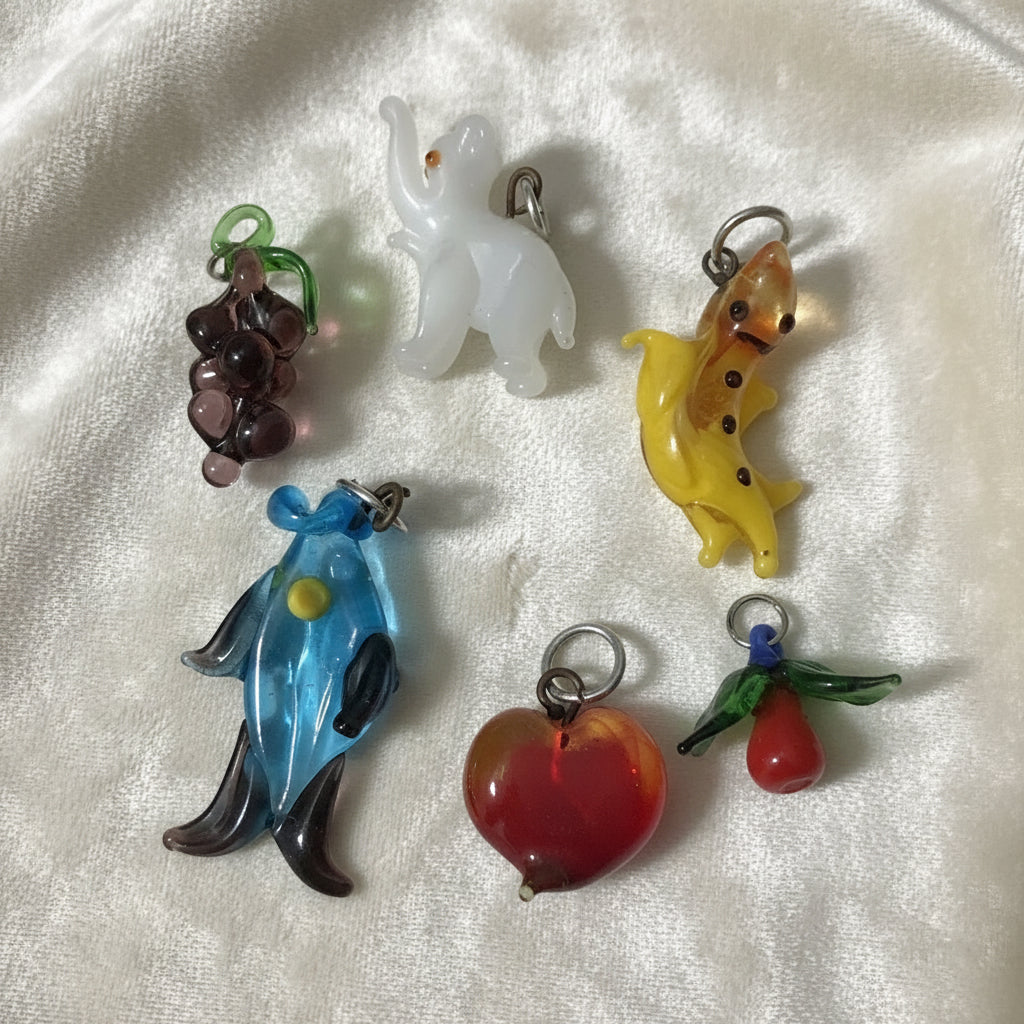 1960s vintage lampwork charms: a white elephant, a salamander, a fruit, a heart, a blue fish, and a grape cluster.
