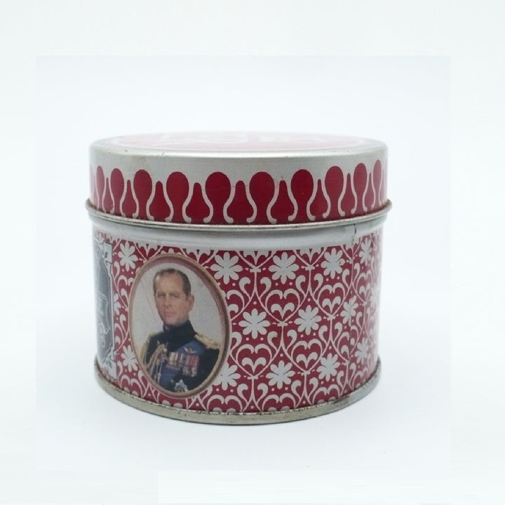 A round metal Matchbox Tin with a red and white floral pattern, featuring a portrait of Prince Albert on the front, set against a plain white background.