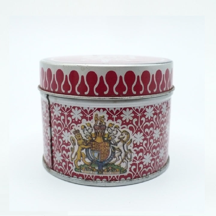 A round metal Matchbox Tin with a red and white floral pattern, featuring a detailed crest on the front and a red and white patterned lid.