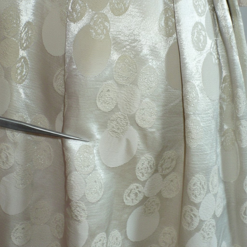 Close-up of the champagne-white jacquard circles pattern and bronze satin waist accent on the 1960s dress. with a pointer showing the tiny mar in fabric.