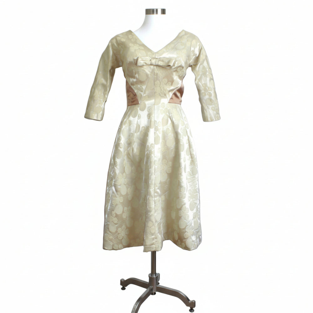 Front angle view of the 1960s Mardi Gras champagne white jacquard dress showcasing its structured A-line silhouette. on a dress form stand.
