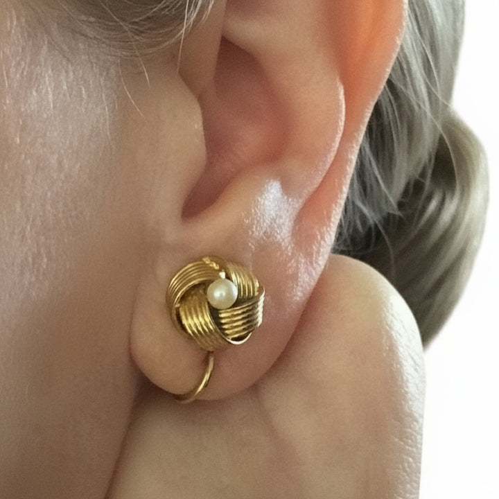 Lover's knot vintage gold earring with pearl detail worn on an ear.