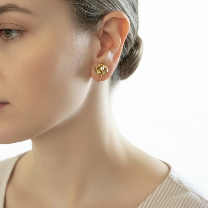 Lover's knot vintage gold earring with pearl detail worn by a person.