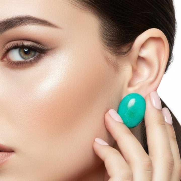 Close-up of a woman wearing a 1980s Vintage Large Oval Cabochon Gemstone Chrysocolla Earrings .on a white background