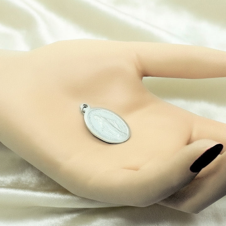 1940s Vintage WWII Eloxal Aluminum Miraculous Medal Pendant on cream velvet background, front view. in palm of hand.