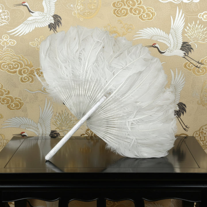 Antique 1910s Zhuge Liang Yu-Shan White Feather Fan Bamboo Stem Handle on a wooden table with a patterned wallpaper background featuring cranes.