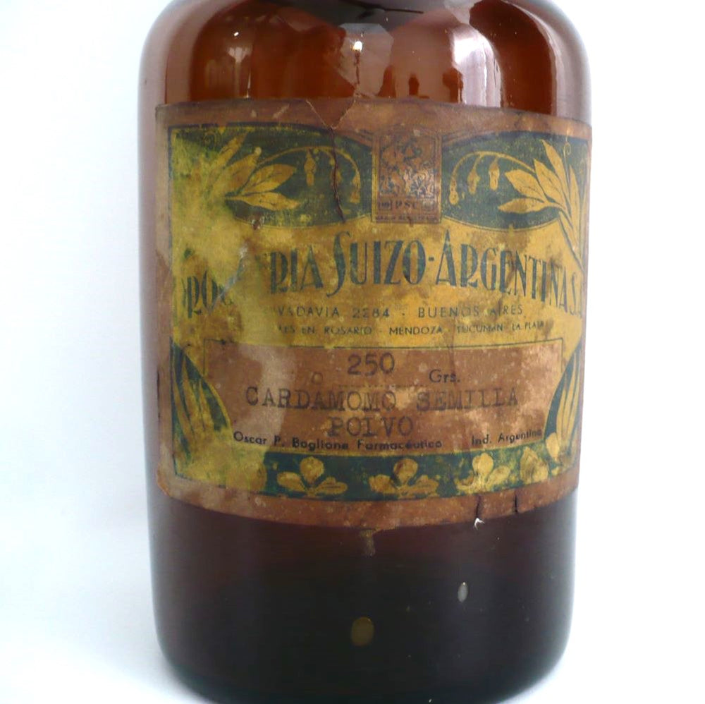 Original paper label of 19th-century hand-blown amber glass apothecary jar with a label indicating it once contained cardamon seed powder. The jar has a dark amber color, a narrow neck, and a round stopper.