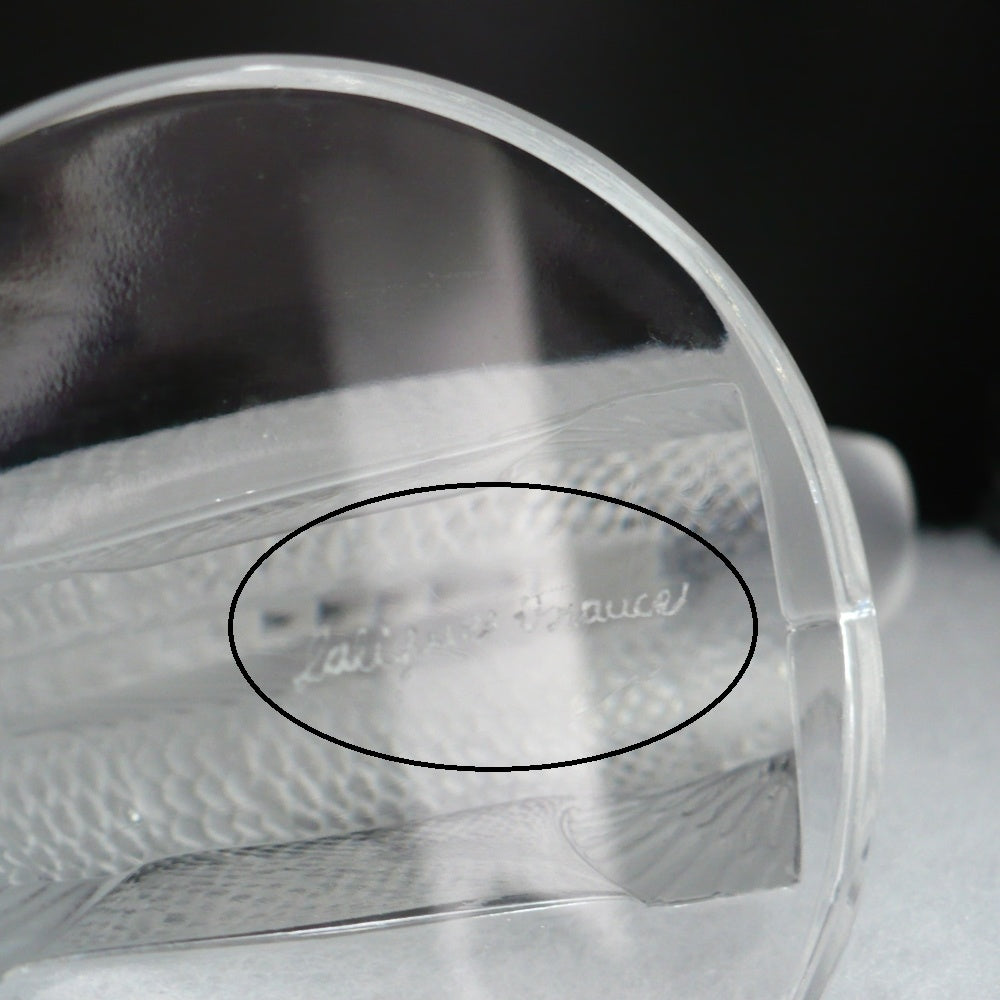 A frosted crystal fish sculpture, Perche Bouchon de Radiateur: Perch Car Mascot, displayed on a clear glass stand against a neutral beige background, base with Lalique  France.