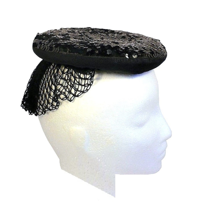 Side profile view of the 1930s black gelatin sequined evening hat on a white mannequin head, clearly showing the rolled brim and veil placement.