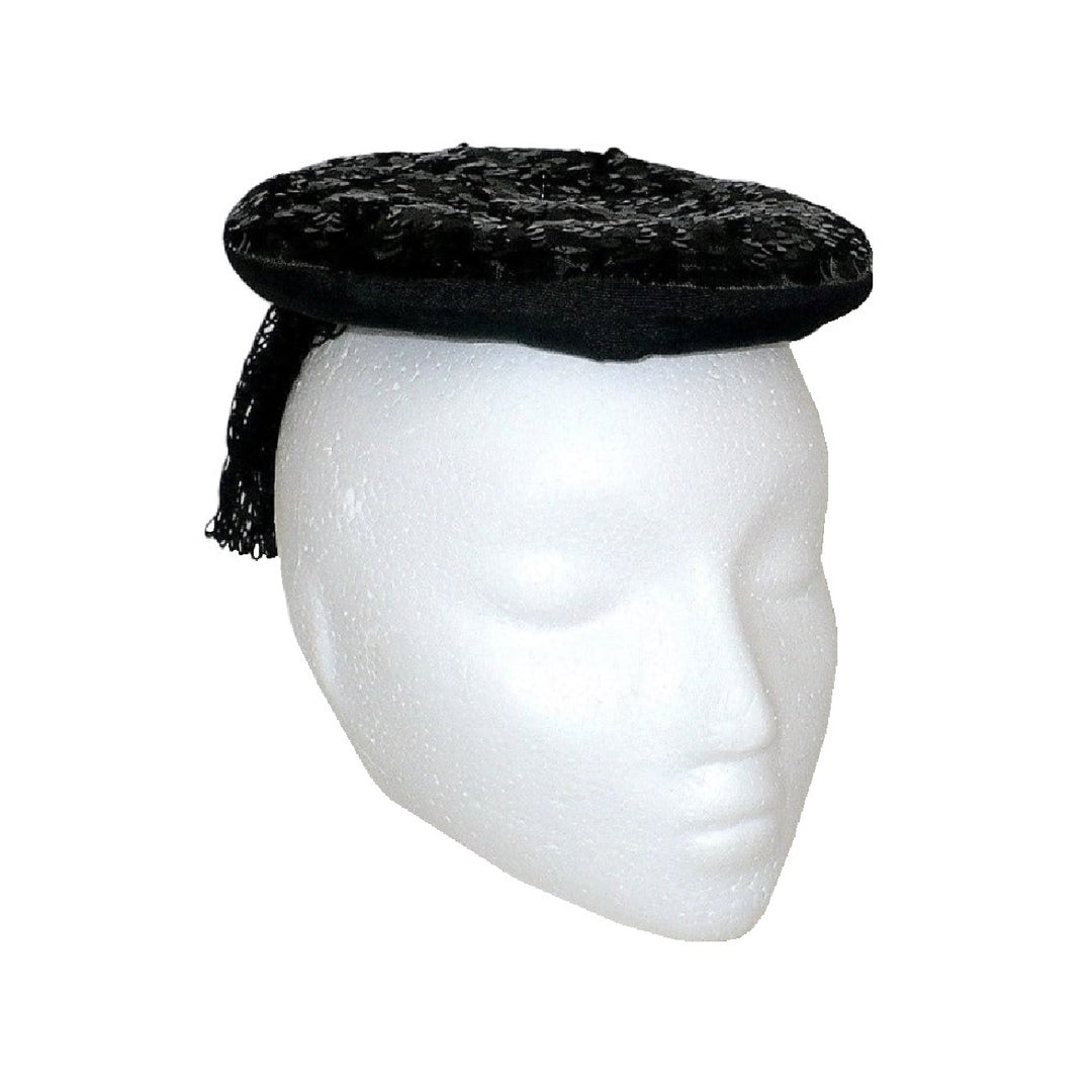 1930s black gelatin sequined percher hat worn on a white mannequin head, viewed from a three-quarter angle to the right, showing the mesh veil draping.