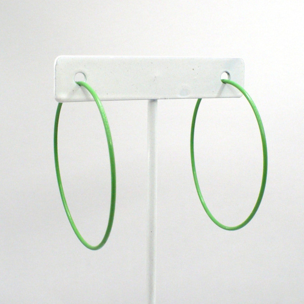 Front-facing view of the 1980s kelly green pop art Memphis style 2-inch hoop earrings displayed on a white T-bar jewelry stand against a neutral background.