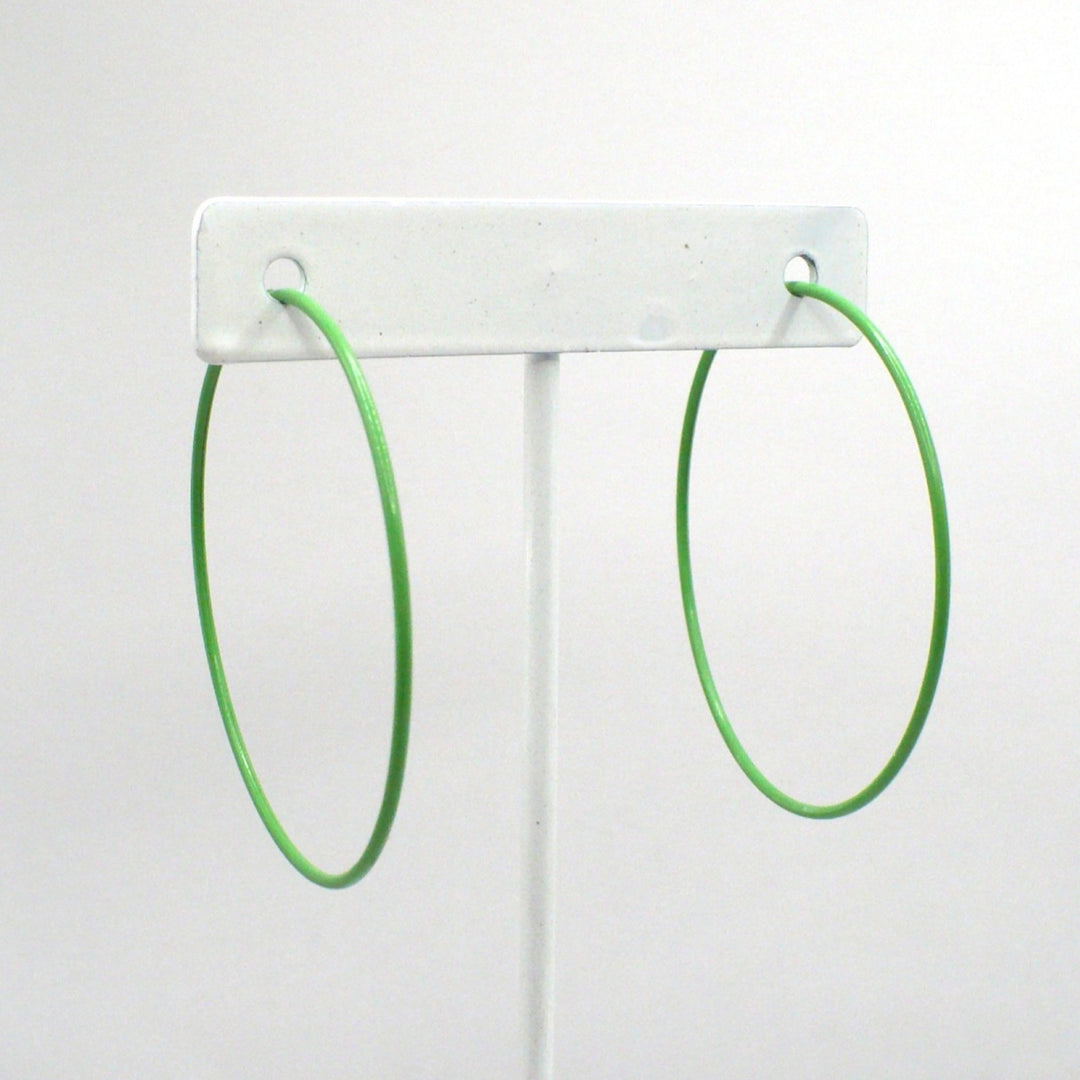 Front-facing view of the 1980s kelly green pop art Memphis style 2-inch hoop earrings displayed on a white T-bar jewelry stand against a neutral background.
