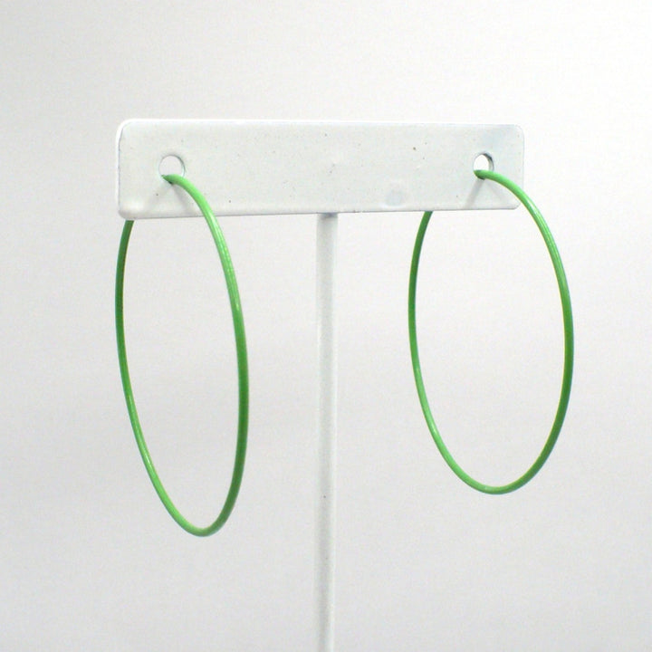 Front-facing view of the 1980s kelly green pop art Memphis style 2-inch hoop earrings displayed on a white T-bar jewelry stand against a neutral background.