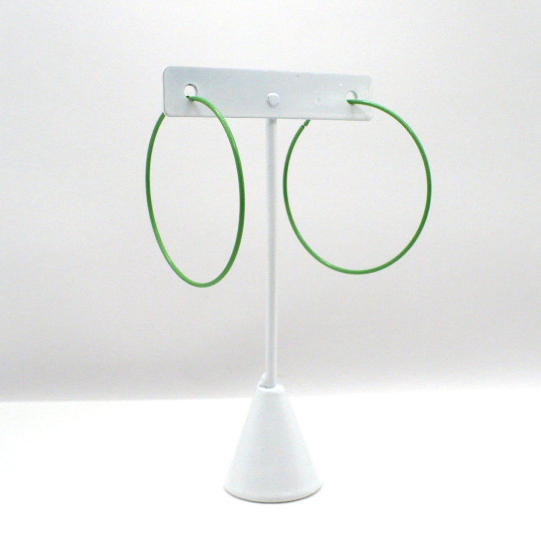 Front-facing view of the 1980s kelly green pop art Memphis style 2-inch hoop earrings hanging on a white T-bar jewelry display stand against a neutral background.

