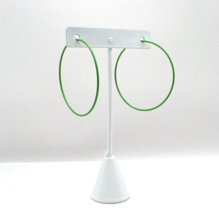 Front-facing view of the 1980s kelly green pop art Memphis style 2-inch hoop earrings hanging on a white T-bar jewelry display stand against a neutral background.

